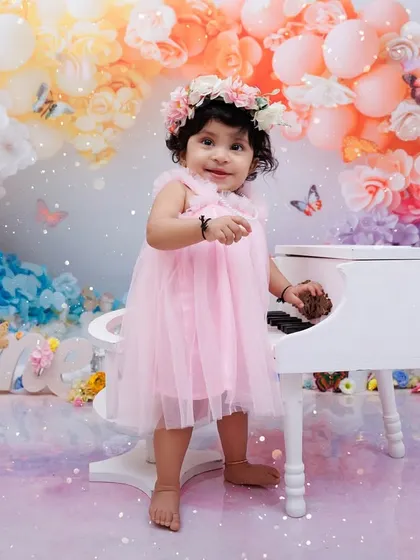 A little pianist plays on a miniature white piano during her whimsical, butterfly-themed first birthday shoot.