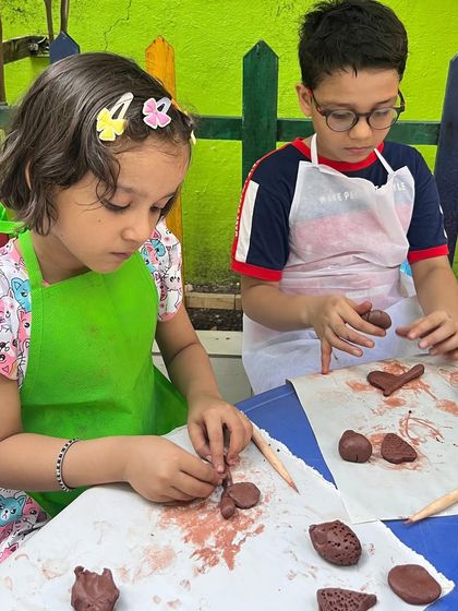 Two young artists working side-by-side, completely absorbed in their terracotta clay projects. This shows the intense concentration that clay work inspires, helping to improve attention span.