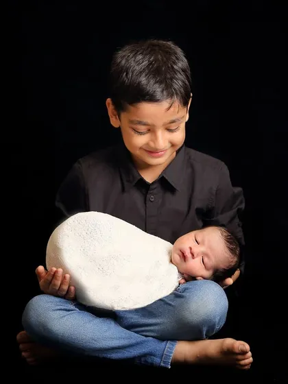 A heartwarming shot of a big brother looking down at his sleeping newborn sibling with a gentle smile. These are the moments that families will treasure forever.