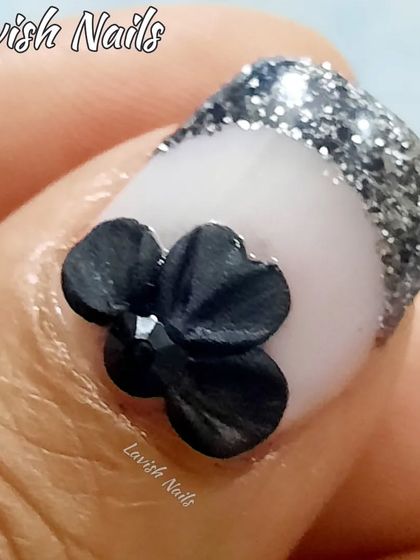 A close-up of a 3D sculpted black bow on a nail with a silver glitter French tip, showcasing the intricate detail of 3D nail art.