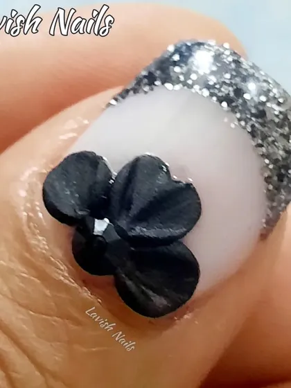 A close-up of a 3D sculpted black bow on a nail with a silver glitter French tip, showcasing the intricate detail of 3D nail art.