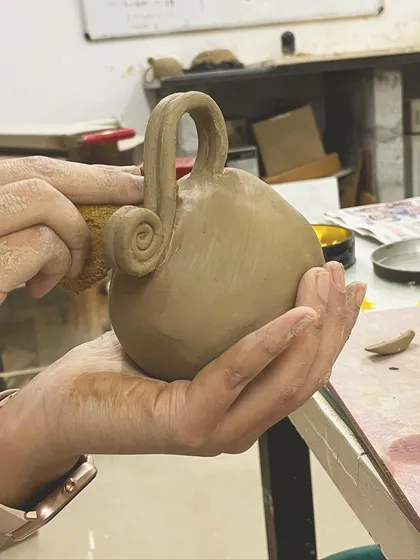 Adding a handle is a key step in mug making. This student is carefully attaching a beautifully swirled handle to their hand-built creation.