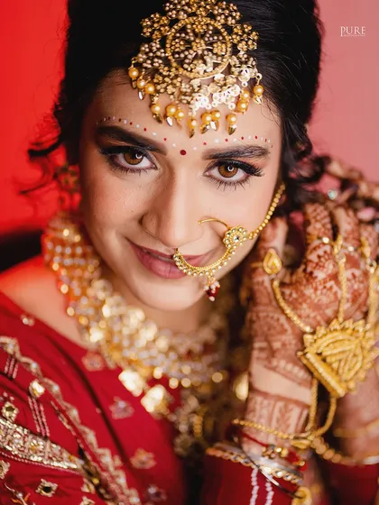 A close-up of the bride adjusting her nath. This candid-style portrait captures a natural gesture and showcases her beautiful henna and traditional jewelry.