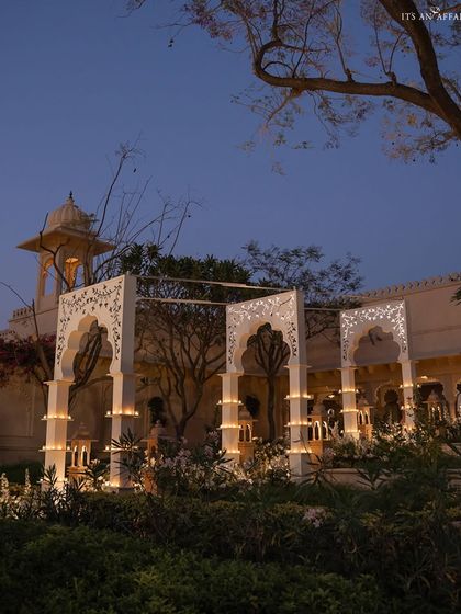 A view of the 'Sheesh Mahal' themed bar at dusk, where intricate white arches and candlelight create a regal atmosphere at The Oberoi Udaivilas.