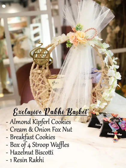 This is my Exclusive Rakhi Basket, a stunning crescent-shaped jute basket filled with a curated selection of treats. It includes Almond Kipferl Cookies, Cream & Onion Fox Nuts, Stroop Waffles, and a complimentary Resin Rakhi.