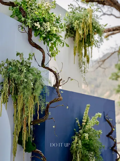 A close-up of the organic floral and branch details on the Mehndi backdrop. The twisting branches and cascading greenery create a beautiful contrast against the clean lines of the blue and white panels.