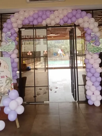 An entrance balloon arch in shades of purple and white for a baby shower. The arch is accented with peacock cutouts to match the event's theme.