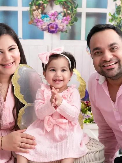 A happy first birthday portrait. The birthday girl, complete with fairy wings, smiles brightly between her parents in this joyful and colorful milestone photo.