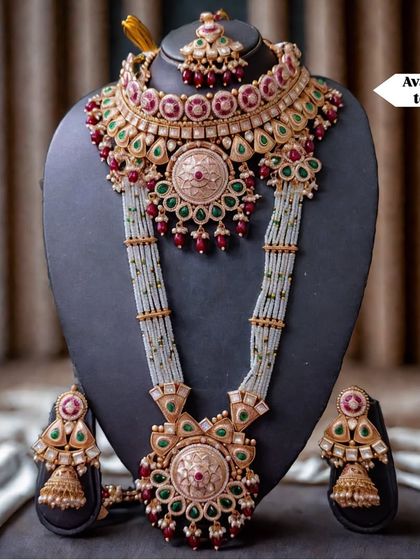 A breathtaking bridal set for sale, featuring intricate kundan work with red and green stones. This complete set, including a choker, rani haar, and earrings, is a perfect investment for your trousseau.