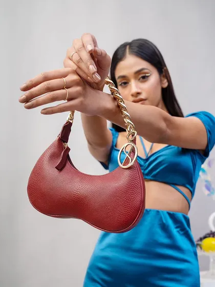 A creative pose where the model displays the Sarjaa handbag on her wrist. This highlights the bag's chain detail and presents it almost like a piece of jewelry.