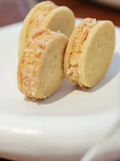 A close-up of almond sandwich cookies on a uniquely shaped white plate. This highlights the beautiful, custom tableware we often use to complement our food.