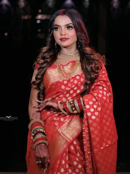A three-quarter portrait showing the rich texture and polka-dot pattern of the red Banarasi saree.
