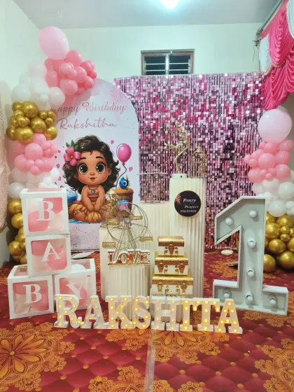A cute and colorful first birthday setup with a Moana-inspired theme, featuring a pink shimmer wall, character art, and a large light-up number '1'.