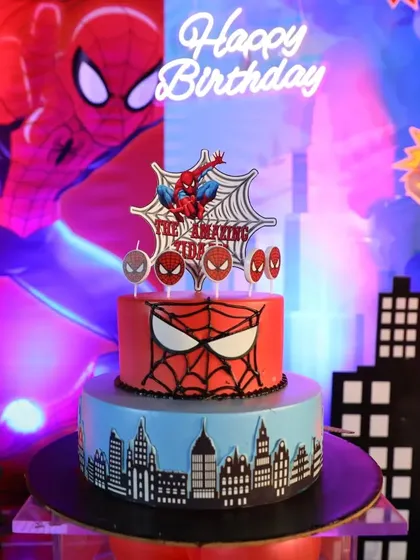A custom two-tier Spider-Man cake, complete with a web design and city skyline, serves as the delicious centerpiece for this superhero birthday party.
