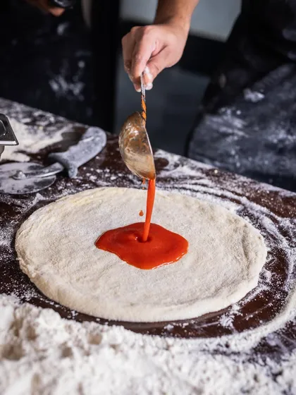 Pizza perfection in the making. The first layer of sauce is carefully spread across the dough.