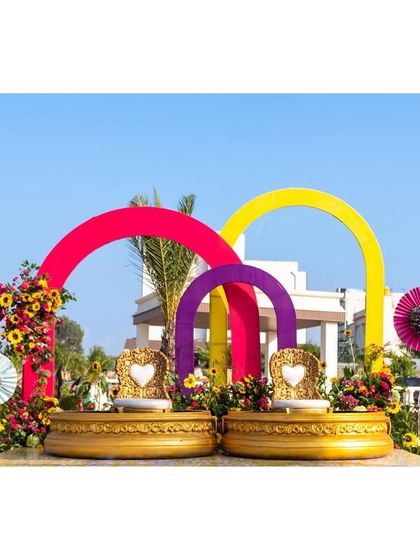 The main seating for a vibrant Haldi ceremony, featuring colorful arches and traditional 'urlis' for the couple, set against a bright blue sky.