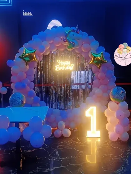 A unicorn-themed first birthday party in a venue with neon lighting, featuring a balloon arch and marquee number.