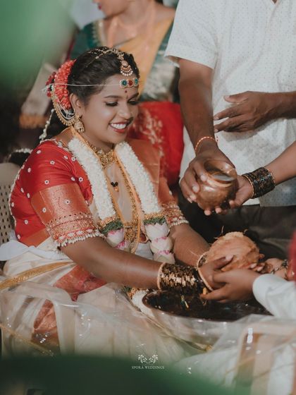 The bride smiling as she participates in a ritual involving a coconut, a symbol of prosperity and blessings.