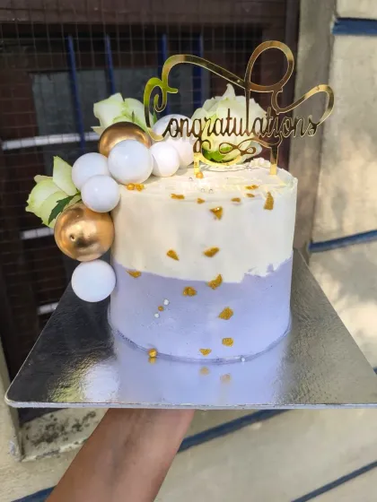 This lilac and gold cake is a dream for any elegant celebration. The combination of soft lavender buttercream, shimmering gold leaf, decorative spheres, and fresh white flowers creates a sophisticated and modern look.