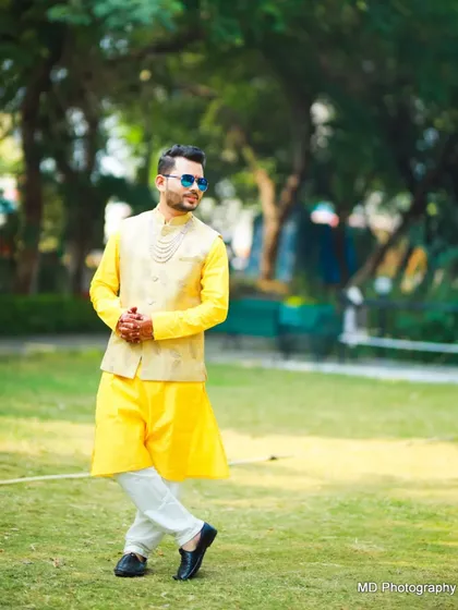 A stylish Haldi look. The groom pairs a bright yellow kurta with a beige waistcoat and cool sunglasses for a fun, modern vibe.