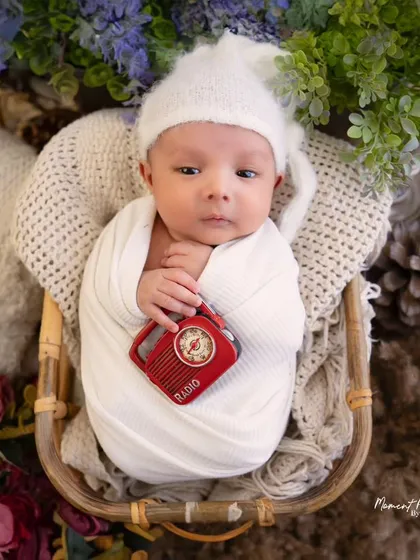 Wide awake and taking it all in. This adorable newborn is holding a tiny prop radio, adding a touch of whimsy to this classic basket pose.