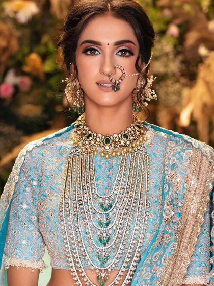 A close-up of a stunning pastel blue bridal look. The makeup is soft and elegant, with a clean winged liner and a neutral lip, allowing the magnificent layered jewellery to be the star.