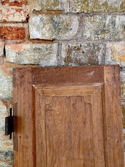 A close-up of a salvaged wooden door panel against an old brick wall. The texture of the wood and the patina of the bricks tell a story of time, which we aim to preserve.