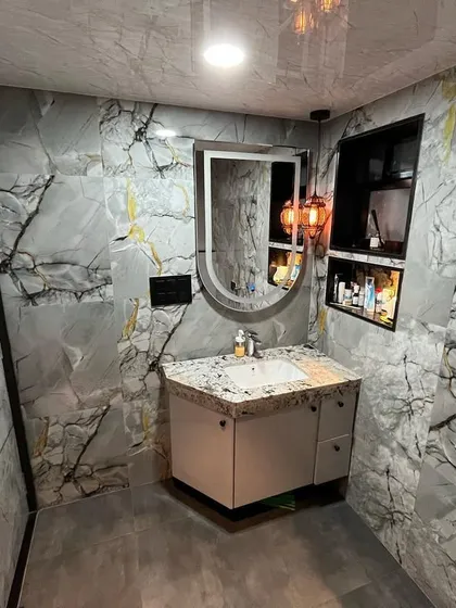 This bathroom uses large grey marble tiles with gold and black veining for a striking look. The space is equipped with a floating vanity, a modern oval mirror, and a built-in wall niche for storage.