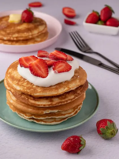 A perfect stack of fluffy pancakes topped with cream and fresh strawberries. This is a classic breakfast shot that always looks delicious.
