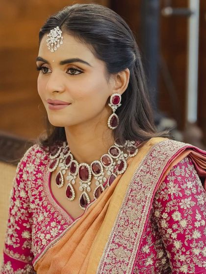A close-up beauty shot of the Pelikuthuru look. The makeup is soft and radiant, letting the statement ruby jewelry and the bride's natural beauty shine.