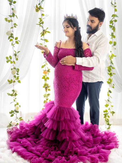 A royal-themed couple's portrait, with the mom-to-be wearing a crown in her magenta gown while her partner embraces her.