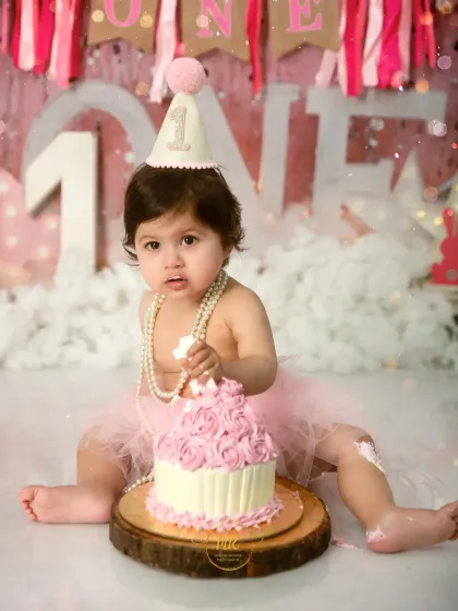 A close-up of a baby girl about to dig into her pink rosette cake during her first birthday cake smash.