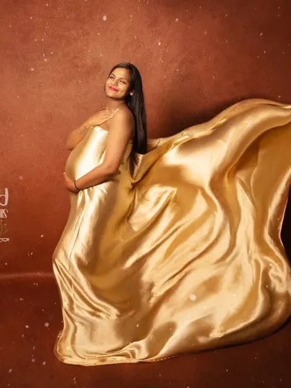 A truly glamorous maternity portrait featuring a solo mom-to-be. The flowing golden satin fabric creates a sense of movement and elegance, making for a dramatic and unforgettable fine-art pregnancy photo.