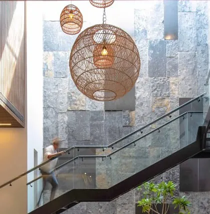 A detail shot of the staircase and double-height stone wall in our Casa Acentuada project. The large, woven pendant lights add a soft, organic texture that contrasts with the hard surfaces.
