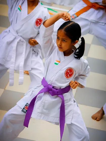A young student demonstrates a powerful high block during an outdoor training session. Her focused expression and sharp form showcase the discipline and technical skill we instill in our karateka from an early age, building both physical strength and mental concentration.