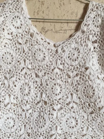 A full view of the classic white lace top on a hanger. The V-neck design and scalloped edges are details I love to perfect. It’s a timeless piece for any wardrobe.