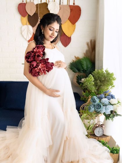 A lovely solo portrait of a mom-to-be in a cream-colored gown, holding a bouquet of deep red flowers that add a pop of color.