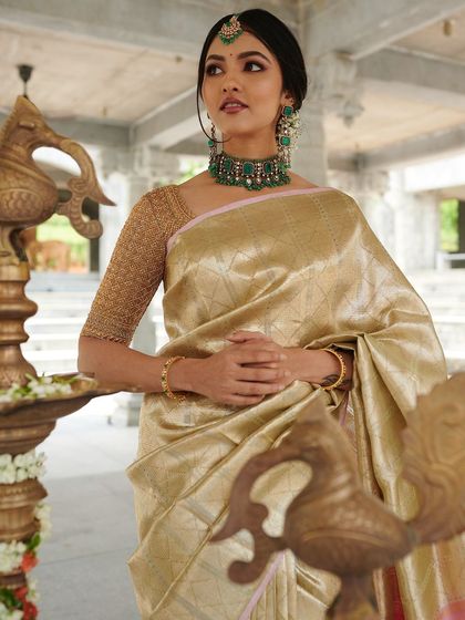 Actress Samikshaa looks stunning in a gold Kanchivaram saree paired with a bespoke hand-embroidered blouse, set against traditional brass lamps.