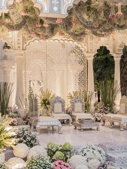 A detailed shot of the mandap stage, highlighting the silver thrones and the lush floral arrangements at the base. The design combines regal seating with soft, natural elements.