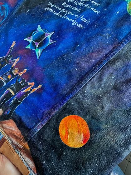 A detailed shot focusing on the hand-lettered lyrics and the celestial bodies painted on the jacket. The fine white script stands out against the deep blue and purple nebula, and the small orange planet adds a pop of color.