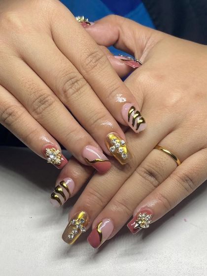 A bold and luxurious set. These square-shaped nails feature a mix of gold chrome, 3D textures, and large, cross-shaped rhinestone clusters.