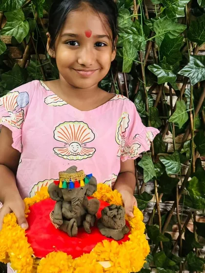 A student with her beautifully decorated clay Ganesha, complete with a colorful hat and a bed of flowers.