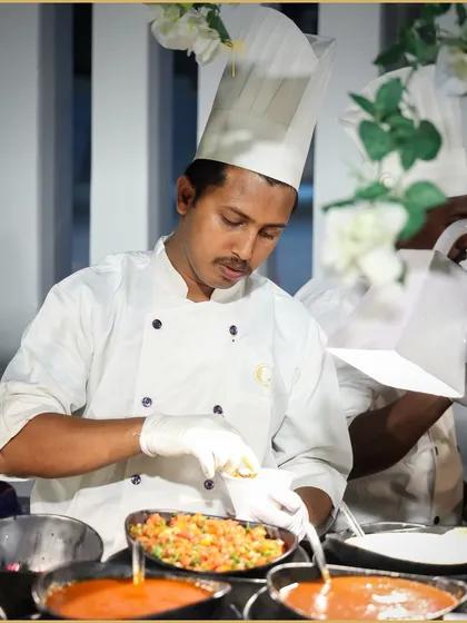 A chef at a live station meticulously adds the final garnish to a dish. This behind-the-scenes shot showcases the attention to detail that goes into every single serving.