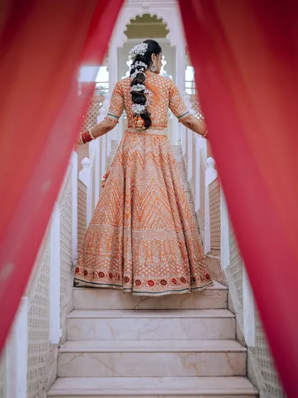 A dramatic and artistic shot of the bride, showcasing the back of her lehenga and her beautiful braided hairstyle.