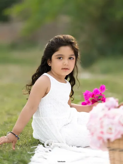 A serene outdoor portrait of a young girl sitting on a blanket in the grass. The soft natural light and her thoughtful expression create a beautiful, timeless image.