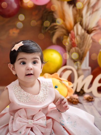 Cuteness loading. A close-up shot of a baby girl in a beautiful pink dress, her curious eyes looking up.