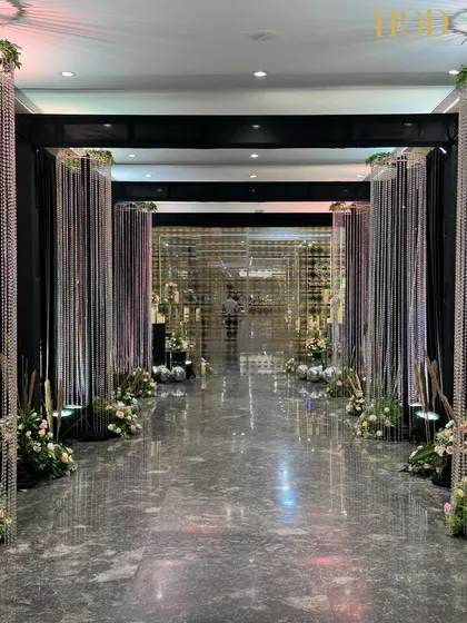 A modern and glamorous hallway created with curtains of sparkling crystals and dark fabric, leading guests down a reflective, polished floor.