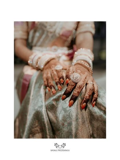 A detailed shot of the bride's hands, adorned with intricate henna, red nail polish, and traditional bangles.