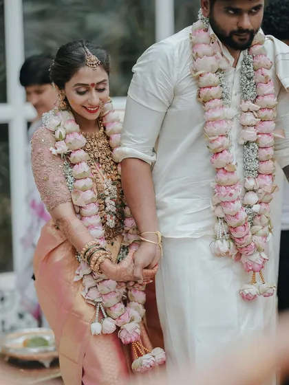 A sweet moment of the couple walking hand-in-hand after a ritual, their garlands of pink lotuses adding a beautiful touch.