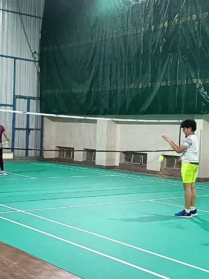 A young player prepares to serve while his partner stands ready. This image captures a moment of focus during a kids' badminton coaching session.